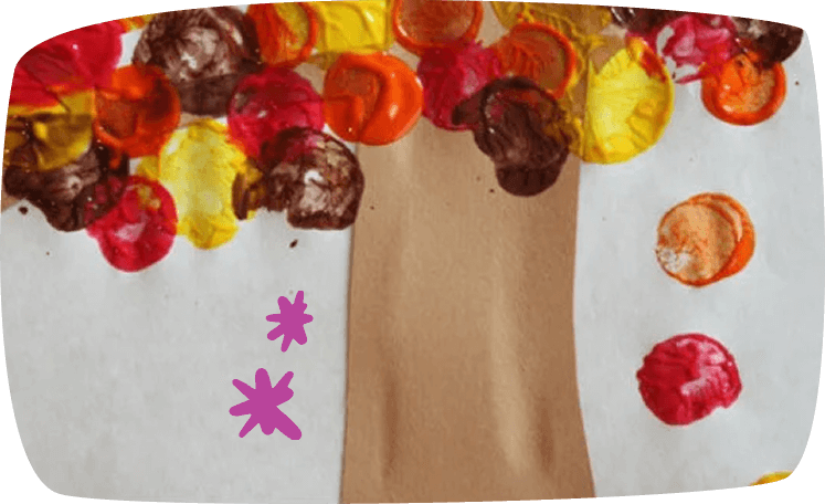 A children's craft artwork showing an autumn tree with a brown paper trunk and colorful circular leaf prints in red, orange, yellow, and brown painted on white paper.