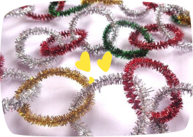 A collection of colorful metallic pipe cleaner rings in silver, gold, red, and green, scattered on a white surface, with two small yellow shapes in the center.
