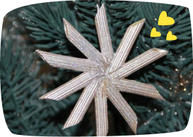A silver glittery star-shaped Christmas ornament hanging on an artificial green Christmas tree.
