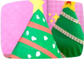 Two handmade cone-shaped Christmas trees decorated with colorful stripes, hearts, and star toppers, set against a pink background.