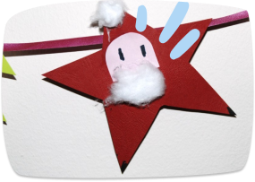 A handmade craft featuring a cute cow figure made from cotton wool and paper, displayed on a red felt star with colorful decorations.