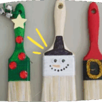 Three paint brushes decorated as Christmas characters, including a Christmas tree, a snowman, and a gift, displayed side by side.